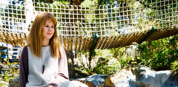 Aliisa istuu kosken äärellä riippusillan edessä.