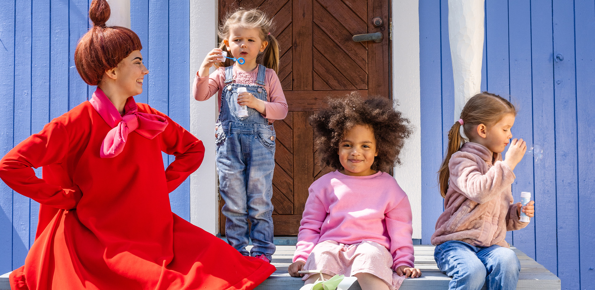 Pikku Myy ja lapset puhaltavat saippukuplia Muumitalon kuistilla.